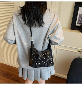 Detail of black pleated shoulder bag with white pearl accents on model in grey outfit