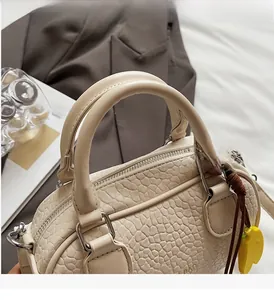 Close-up of beige bowling handbag featuring embossed leather texture and silver zipper detail