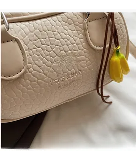 Close-up of beige crocodile-textured handbag with yellow banana charm and embossed logo