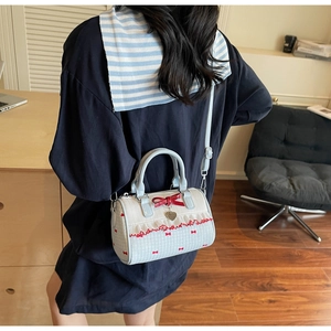 Detail of blue cylinder bag with red bows and heart pendant worn by a model