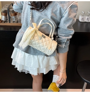 Détail du sac cylindrique beige matelassé avec nœud en dentelle et chaîne métallique
