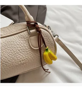 Detail of beige wavy textured handbag with a playful yellow banana charm and brand logo