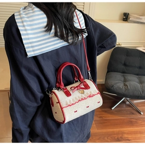 Detail view of cream Boston bag with red bow accents and gold heart pendant decoration