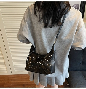 Detail of black pleated hobo bag featuring silver rivet studs worn by a model in casual setting