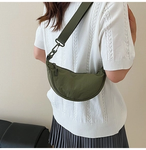 Military green crescent shoulder bag with wide strap worn by model on beige background
