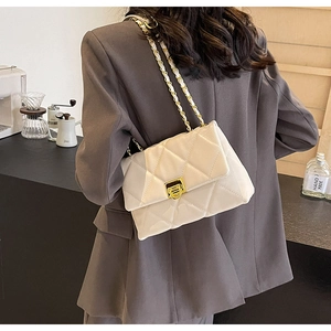 Detail of white quilted crossbody bag with gold chain strap and rotary lock worn by model