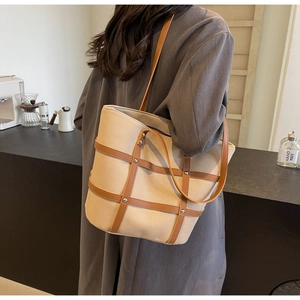 Detail of canvas tote bag with brown leather lattice and silver studs on a female model