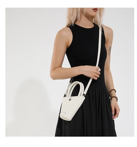 Gros plan d'un sac seau blanc en cuir grainé avec design asymétrique et bandoulière