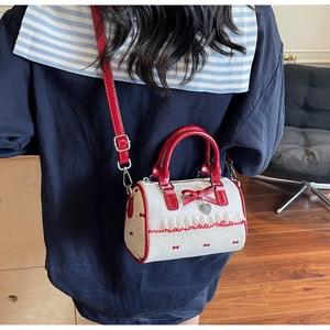 Detail of Boston bag showing red leather handle, bow prints, and silver heart pendant