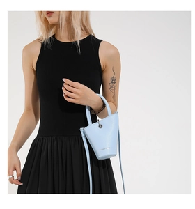 Petit sac seau bleu clair en cuir grainé porté avec une robe noire sans manches