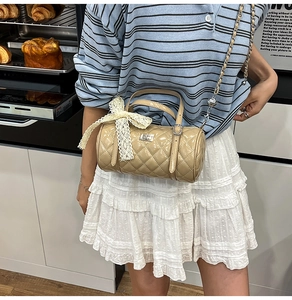 Détail du sac cylindre beige matelassé avec nœud en dentelle et bandoulière en chaîne métal