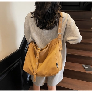 Detail view of mustard yellow canvas tote bag with adjustable strap worn by a model