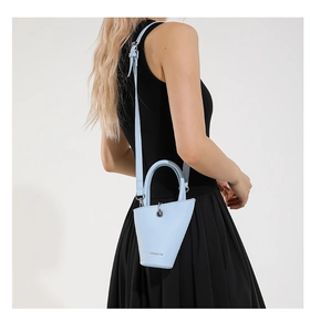 Détail du sac seau bleu clair en cuir grainé porté à l'épaule par un mannequin en studio