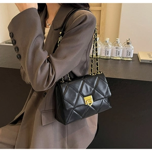 Détail d'un sac bandoulière en cuir matelassé noir avec chaîne dorée et fermoir carré