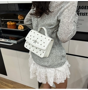 Detail of white quilted crossbody bag with silver studs and star emblem on flap