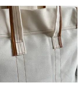 Gros plan des coutures renforcées et de la bandoulière en cuir du sac cabas en toile