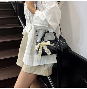 Détail du sac cylindrique noir matelassé avec nœud en dentelle et bandoulière chaîne
