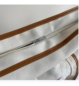 Détail du zip en métal argenté sur un sac en toile crème avec bordures en cuir marron