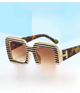 Detail of square sunglasses featuring black and yellow stripes with gold T-shaped metal hinges