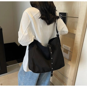 Detail of black canvas tote bag with metal eyelets on strap styled in casual setting
