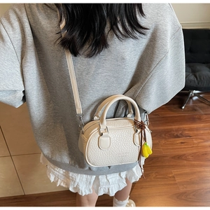 Detail of a creamy white mini crossbody bag with lychee texture and a yellow banana charm
