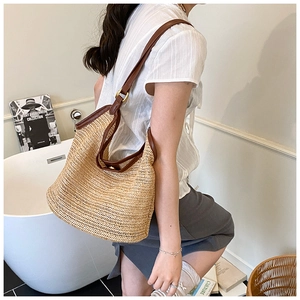 Detail of hand-woven straw shoulder bag with brown leather strap in a chic indoor setting