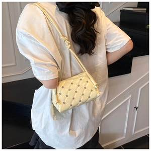 Macro detail of creamy yellow quilted crossbody bag with rhinestone studs and knotted strap
