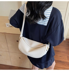 Detail of white pebbled leather crescent bag featuring golden hardware and sleek zipper