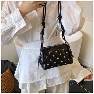 Detail of black shell crossbody bag with diamond quilting and metallic rivet accents