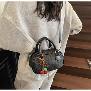 Close-up of black lychee leather bowling bag with a cherry charm and crossbody strap