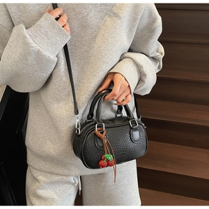 Detail of black litchi leather mini boston bag with a cute red cherry charm on a model