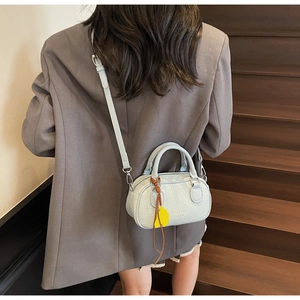 Close-up of a light blue textured pillow bag with a yellow leather pendant on a staircase