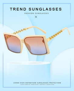 Detail view of square sunglasses with cream frame and gold metal chain link temples