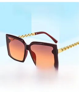 Detail of square oversized sunglasses with orange gradient lenses and gold chain temples