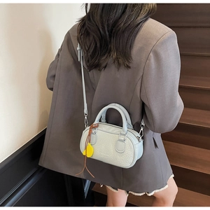 Close-up of light blue textured leather crossbody bag with yellow charm on a model