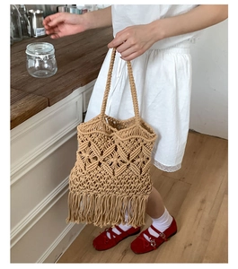 Detail of handmade woven straw tote bag featuring bohemian tassels and hollow diamond pattern