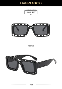 Close-up of black square sunglasses with industrial hollow-out design and grey lenses