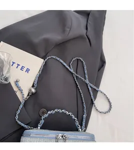 Detail of light blue tweed crossbody bag with silver chain strap and decorative metal ball
