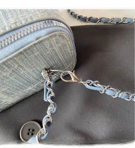 Detailed macro shot of silver hardware and woven chain strap on a blue textured crossbody bag