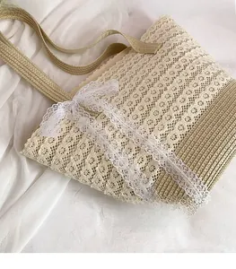 Detail of beige straw tote bag featuring white floral lace overlay and decorative bow
