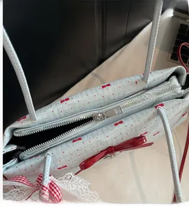 Dettaglio della cerniera argentata e del fiocco rosso sulla borsa tote azzurra