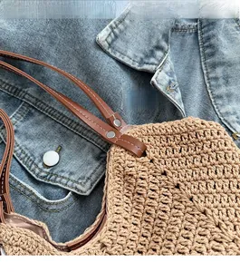 Close-up of hand-woven straw tote with premium brown leather strap and silver rivets