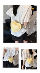 Détail du sac bandoulière coeur crème avec chaîne dorée porté par une personne