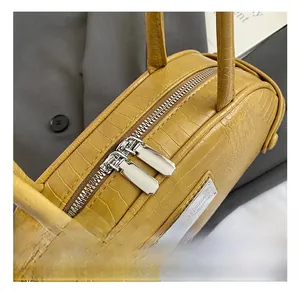 Detail of mustard yellow crocodile pattern handbag with dual metal zippers and logo plate
