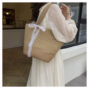 Close-up of hollow straw woven tote bag featuring a large white lace bow decoration