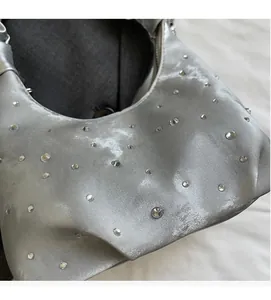 Detailed close-up of silver satin handbag fabric with shiny rhinestones and soft pleats