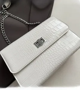 Detail of white crocodile pattern crossbody bag with silver chain and metal twist lock