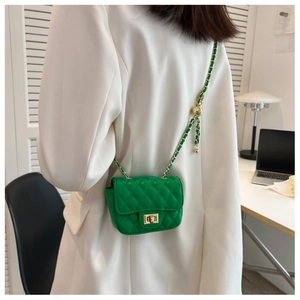 Detail of green quilted mini crossbody bag with gold chain strap worn over white blazer