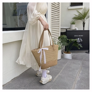 Close-up of woven straw tote bag with elegant white lace bow detail for summer