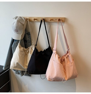 Three textured tote bags in cream, black, and pink hanging on wooden wall hooks